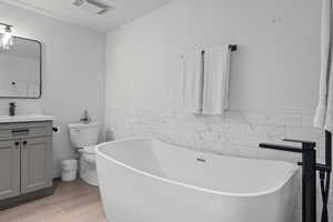 Bathroom with toilet, tile walls, vanity, a tub, and hardwood / wood-style flooring