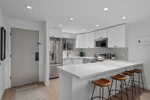 Kitchen with a breakfast bar, sink, appliances with stainless steel finishes, kitchen peninsula, and white cabinets