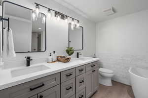 Bathroom featuring wood-type flooring, tile walls, a tub to relax in, vanity, and toilet