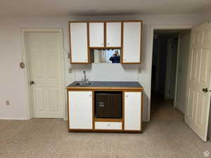 Kitchen featuring white cabinetry, light colored carpet, and sink