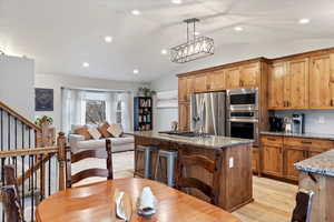 Kitchen with pendant lighting, lofted ceiling, stainless steel appliances, light stone countertops, and light wood-type flooring