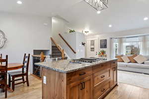 Kitchen featuring light hardwood / wood-style flooring, a kitchen island, a notable chandelier, stainless steel gas stovetop, and light stone countertops