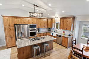 Kitchen featuring sink, appliances with stainless steel finishes, light stone counters, a kitchen island, and decorative light fixtures