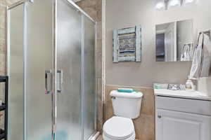 Bathroom featuring an enclosed shower, vanity, tile walls, and toilet