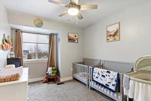 Bedroom with a nursery area, light colored carpet, and ceiling fan