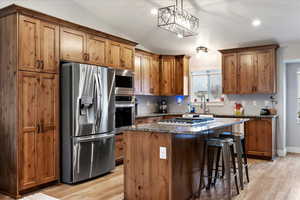 Kitchen featuring a kitchen bar, dark stone counters, hanging light fixtures, a center island, and stainless steel appliances