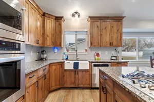 Kitchen with new, farmhouse sink, light stone counters, a textured ceiling, stainless steel appliances, and light hardwood / wood-style floors