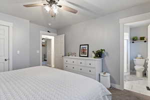 Carpeted bedroom featuring connected bathroom and ceiling fan