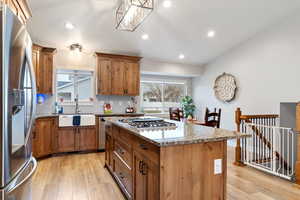 Kitchen featuring farm house sink, light stone counters, a center island, light wood-type flooring, and stainless steel appliances