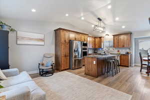 Kitchen featuring lofted ceiling, appliances with stainless steel finishes, hanging light fixtures, a kitchen island, and a kitchen bar