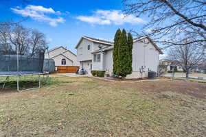 Rear view of property featuring central AC unit, a trampoline, and a lawn