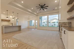 Unfurnished living room featuring a tray ceiling, sink, ceiling fan with notable chandelier, and light hardwood / wood-style flooring