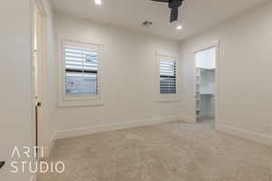 Unfurnished bedroom featuring multiple windows, a walk in closet, light colored carpet, and ceiling fan