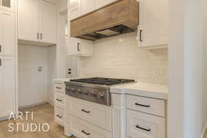 Kitchen featuring custom exhaust hood, light stone counters, white cabinetry, light wood-type flooring, and stainless steel gas stovetop