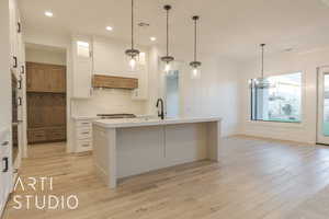 Kitchen featuring extractor fan, white cabinetry, sink, decorative backsplash, and a center island with sink