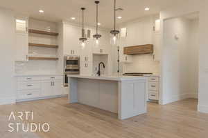 Kitchen with white cabinetry, appliances with stainless steel finishes, an island with sink, and pendant lighting