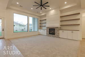 Unfurnished living room with ceiling fan, a fireplace, a raised ceiling, and light hardwood / wood-style floors