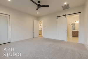 Unfurnished bedroom featuring ensuite bathroom, a barn door, and light colored carpet