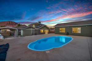 Pool at dusk featuring a carport, a mountain view, and a patio area