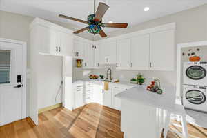 Kitchen featuring light stone counters, light hardwood / wood-style flooring, kitchen peninsula, stacked washing maching and dryer, and white cabinets