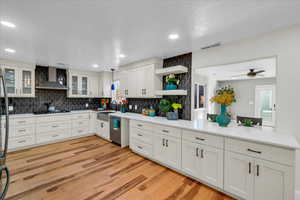 Kitchen with white cabinetry, dishwasher, wall chimney range hood, light hardwood / wood-style floors, and backsplash