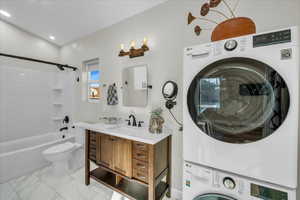 Full bathroom with vanity, stacked washer / drying machine, shower / bathtub combination, and toilet