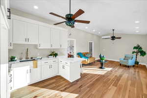 Kitchen with lofted ceiling, kitchen peninsula, a wall unit AC, light hardwood / wood-style floors, and white cabinets