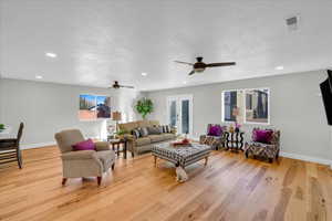 Living room with ceiling fan, french doors, a textured ceiling, and light wood-type flooring