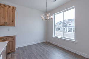 Unfurnished dining area featuring a healthy amount of sunlight, wood finished floors, and a notable chandelier