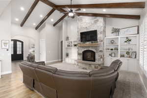 Living room with a stone fireplace, high vaulted ceiling, beamed ceiling, light hardwood / wood-style flooring, and french doors