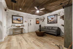 Living room featuring ceiling fan, brick wall, wooden ceiling, and light hardwood / wood-style floors