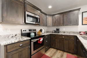 Kitchen with appliances with stainless steel finishes, dark brown cabinetry, light hardwood / wood-style floors, light stone countertops, and a textured ceiling