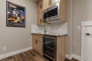 Kitchen with sink, wine cooler, stainless steel microwave, light stone countertops, and decorative backsplash