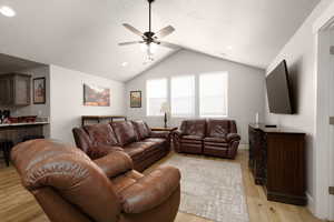 Living room with lofted ceiling, ceiling fan, light hardwood / wood-style flooring, and a textured ceiling