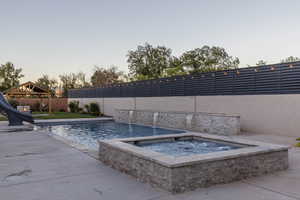 Pool at dusk featuring a gazebo, a water slide, an in ground hot tub, and a patio