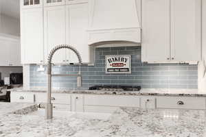 Kitchen featuring white cabinetry, backsplash, light stone countertops, and stainless steel gas stovetop