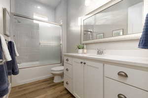 Full bathroom with wood-type flooring, combined bath / shower with glass door, vanity, and toilet