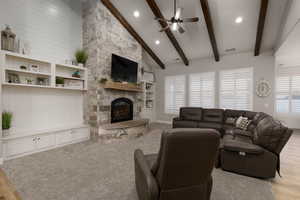 Living room with a stone fireplace, high vaulted ceiling, light hardwood / wood-style flooring, beamed ceiling, and ceiling fan