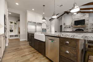 Kitchen with appliances with stainless steel finishes, decorative light fixtures, sink, white cabinets, and light stone counters