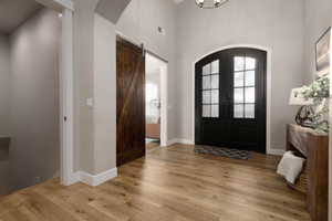 Foyer with a barn door, a towering ceiling, light wood-type flooring, and french doors