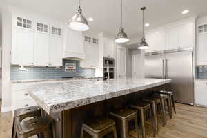 Kitchen featuring white cabinetry, a kitchen breakfast bar, hanging light fixtures, built in appliances, and a spacious island