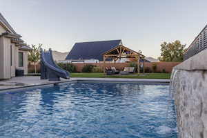 View of swimming pool featuring a water slide, a gazebo, a patio, central AC unit, and an outdoor hangout area