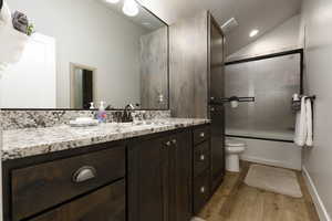 Full bathroom featuring lofted ceiling, hardwood / wood-style floors, bath / shower combo with glass door, vanity, and toilet