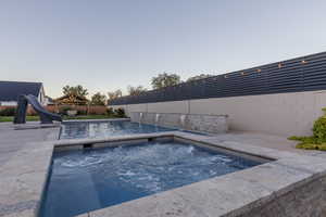 Pool at dusk featuring pool water feature, a gazebo, a water slide, and an in ground hot tub