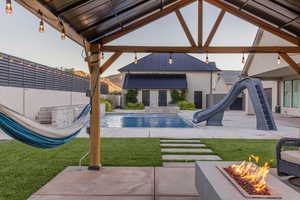 View of pool featuring pool water feature, a water slide, an outdoor structure, an outdoor fire pit, and a patio area