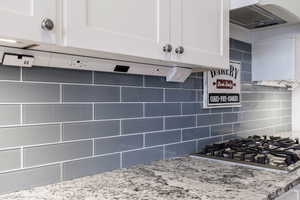 Kitchen featuring stainless steel gas stovetop, white cabinetry, backsplash, and light stone counters