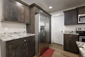 Kitchen featuring light stone counters, dark brown cabinetry, appliances with stainless steel finishes, and light wood-type flooring