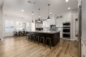 Kitchen featuring a center island with sink, light stone counters, a kitchen bar, decorative light fixtures, and custom exhaust hood