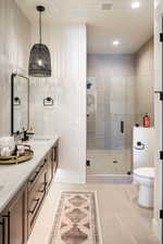 Bathroom with a shower with door, vanity, tile patterned floors, and toilet