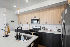 Kitchen with appliances with stainless steel finishes, decorative light fixtures, sink, and light brown cabinets